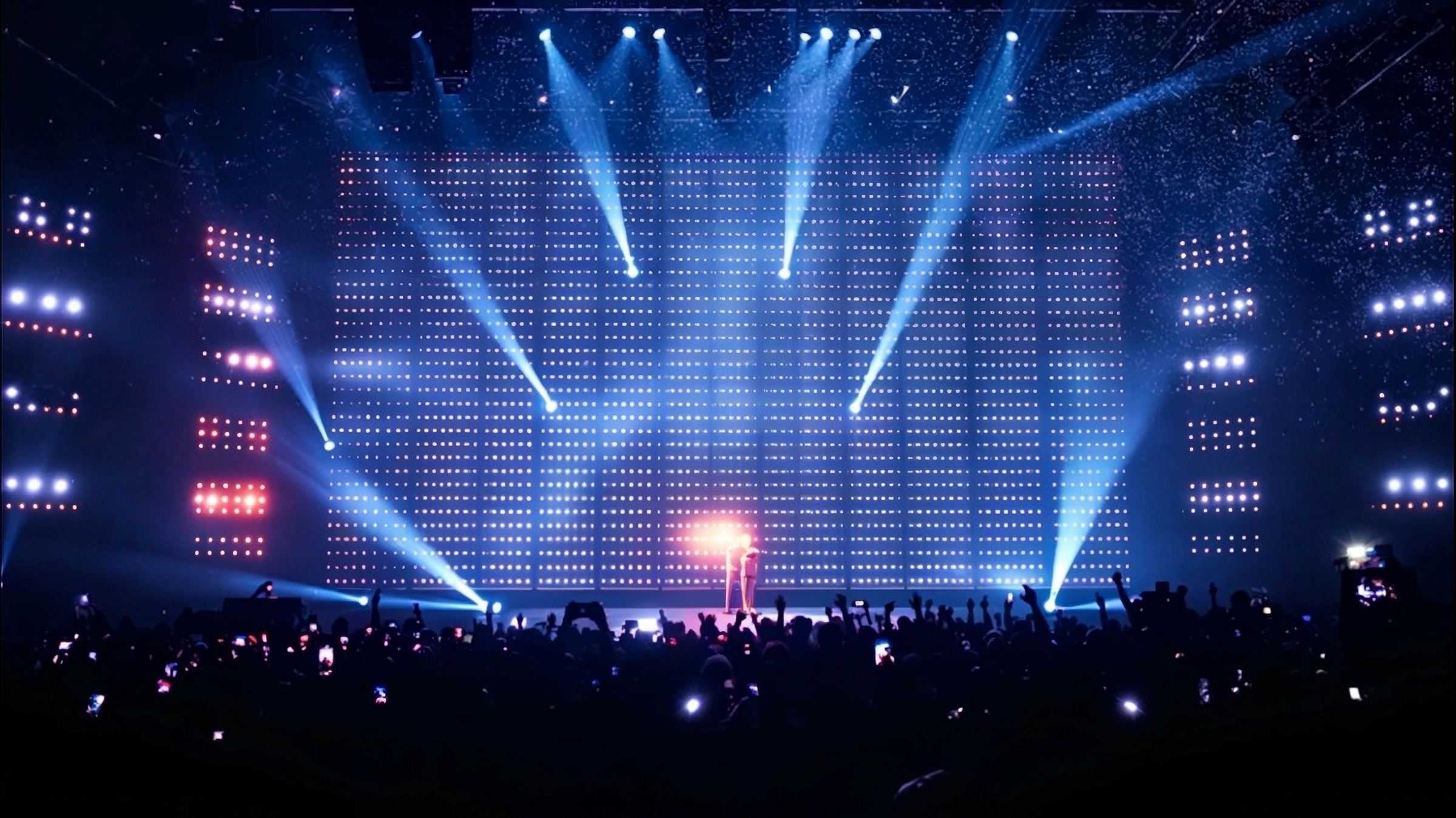 A concert stage lit in blue in front of a packed arena